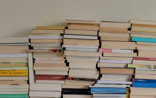 Fotografía a color de una pila de libros apoyados en una pared blanca