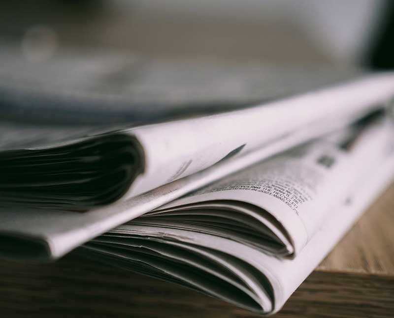 noticias-sector-editoriales_dactilos-2 Fotografía a color de una pila de diarios sobre un mesa de madera