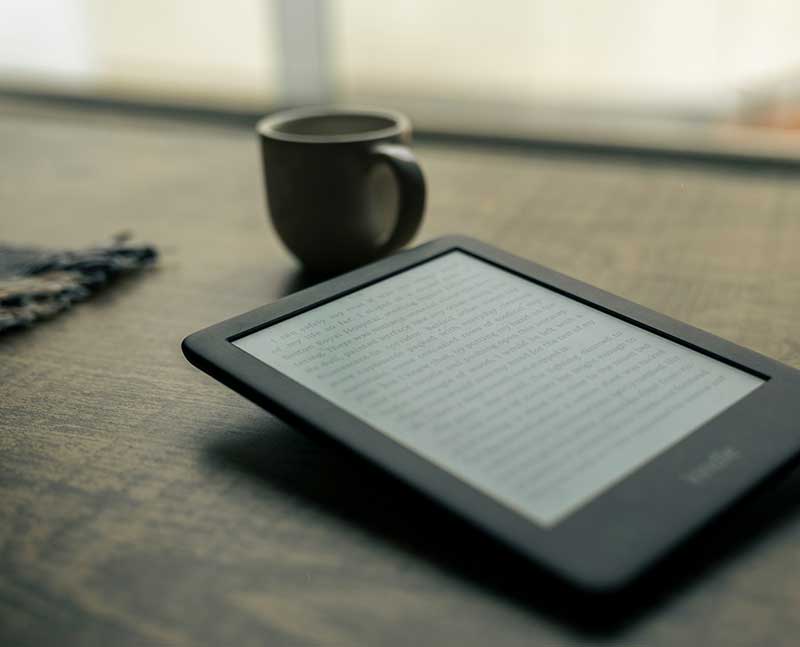Fotografía a color de un e-book junto a una taza sobre una mesa